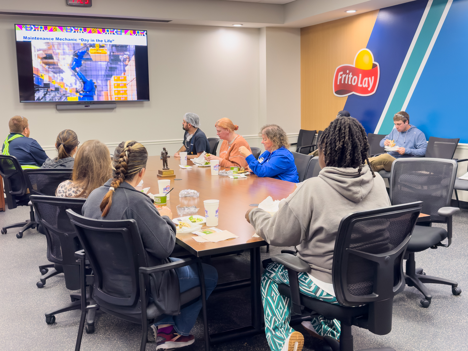 Educators sitting around a board room table at Frito-Lay watching a video about their facility