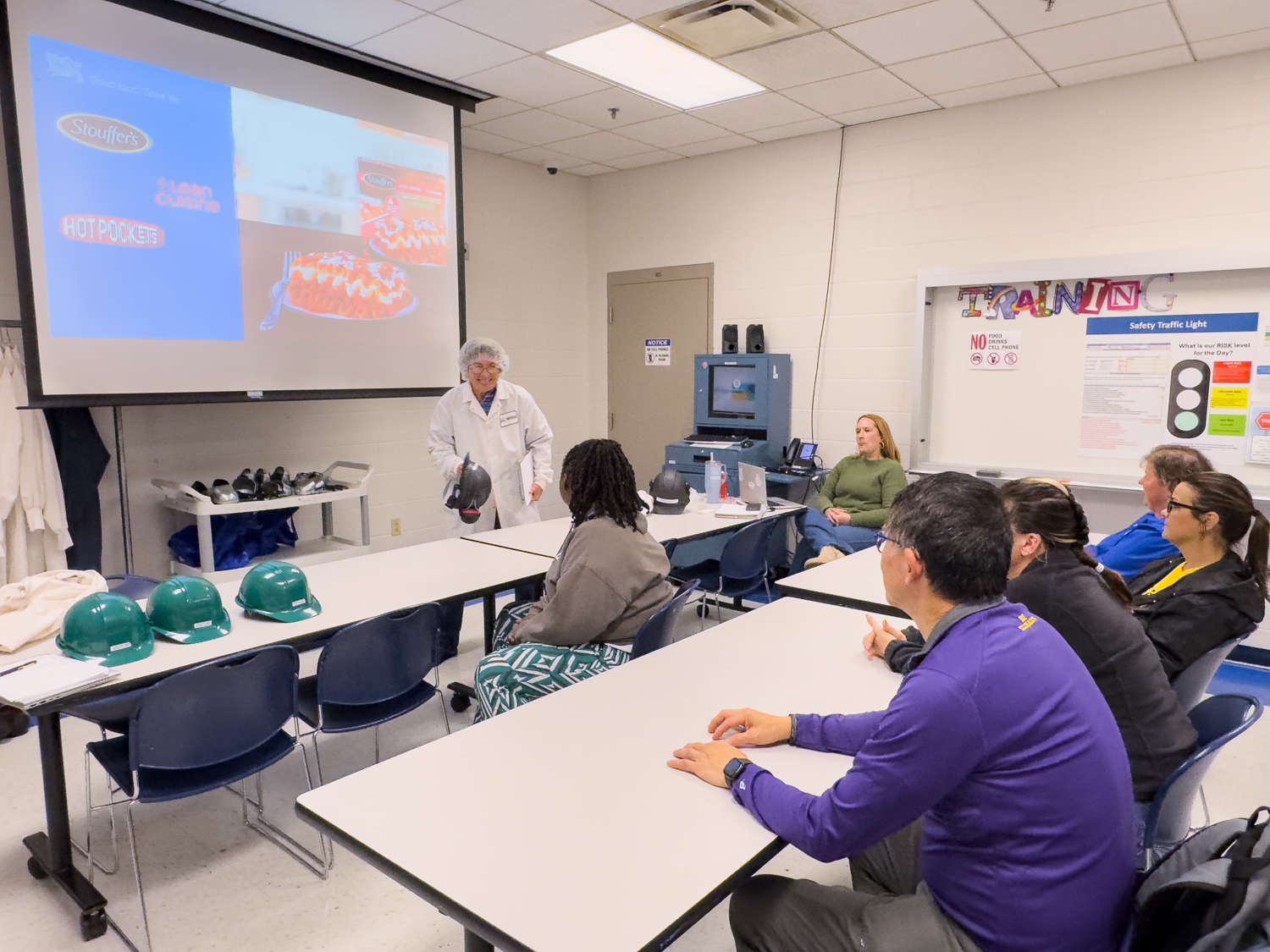 Educators sitting in a room at Nestle watching a PowerPoint and listening to an employee in PPE gear talk to them