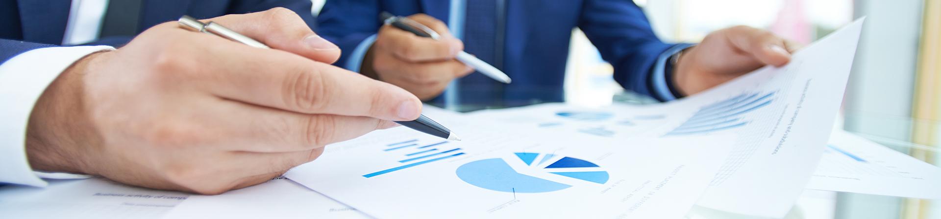 Closeup of businessmen's hands holding pen and documents with data charts on them