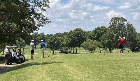 Golf player swinging club as others watch him