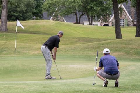 Golfer watches ball he just putted as another player watches from behind.