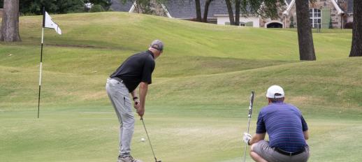 Golfer watches ball he just putted as another player watches from behind.